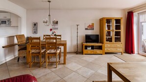 Una sala de estar con una mesa de comedor, sillas, un televisor, un mueble y una zona de cocina.