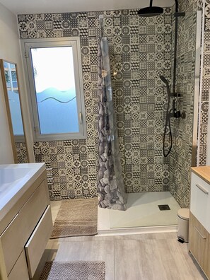 A bathroom with patterned tiles, a shower, a window with a view, and wooden cabinets.