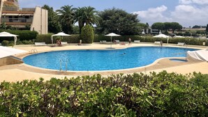 Une piscine à l’eau d’un bleu cristallin, entourée de chaises longues et de parasols, avec un bâtiment visible au loin.