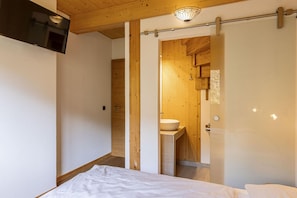 A bedroom with a bed, a wooden ceiling, and a sliding door leading to a bathroom with a sink. - Chalet with panoramic sauna (Schladming - Pichl, Ennstal)