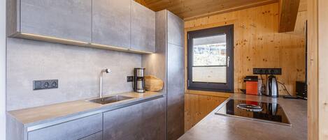 A modern kitchen with grey cabinets, a wooden ceiling, and a window providing natural light.