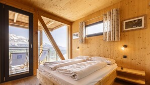 A wooden cabin bedroom with a bed, a window with curtains, a picture on the wall, and a view of mountains through the window. - Chalet with panoramic sauna (Schladming - Pichl, Ennstal)