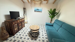 A living room with a blue sofa, a wooden coffee table, a TV on a wooden cabinet, a plant, and a painting on the wall.