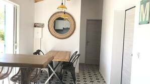 A dining area with a wooden table and chairs, a woven mirror, and a yellow pendant light.