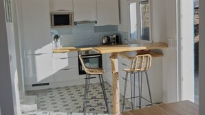 A modern kitchen with white cabinets, a wooden ceiling, and a tiled floor. There are two bar stools and a dining table.