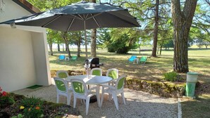 En udendørs terrasse med bord og stole, grill og et overdækket område med parasol.