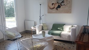En moderne stue med en hvid sofa, et sofabord og to stole med metalstel. Et stort maleri af et strandmotiv hænger på væggen.