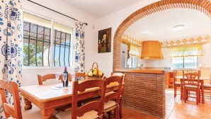 Een eethoek met een bakstenen muur, houten stoelen, een tafel en een keuken met een aanrecht.