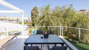 Une terrasse avec une table et des chaises, un pot de fleurs et une vue sur une piscine et des bâtiments.