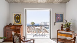 Une pièce avec vue sur la mer, un meuble en bois, deux chaises, une petite table et deux œuvres d’art encadrées.