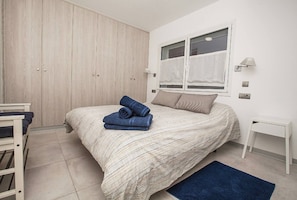 A bedroom with a bed, a wardrobe, a bedside table, and a window with curtains.