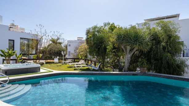 A swimming pool with a hot tub, lounge chairs, and a grassy area with trees.