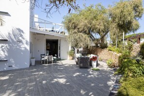 Um pátio moderno ao ar livre com assentos, uma pérgola e uma grande árvore.