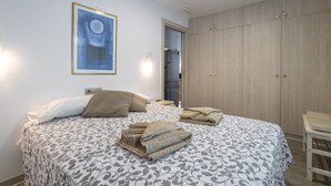 A bedroom with a bed, a wardrobe, a framed picture on the wall, and a door leading to a kitchen.