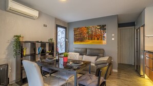 A modern living room with a dining area, a sofa, a painting, and a bookshelf.