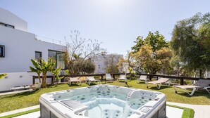 A hot tub in a backyard with a modern house, a wooden fence, and lounge chairs.