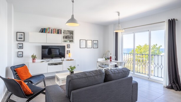 Una sala moderna con sofá, televisor y comedor, con un balcón y vistas.