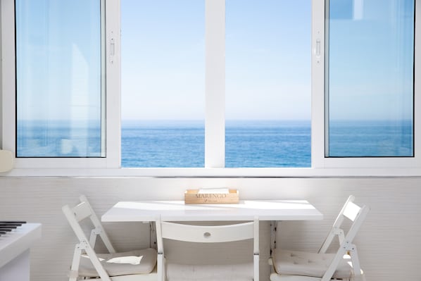 A white desk with a 'MARENGO' sign, two white chairs, and a view of the sea through large windows.