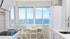 Et moderne køkken med havudsigt, hvide skabe, en indbygget ovn og et spiseområde med bord og stole.