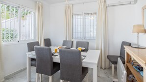 Un coin repas avec une table blanche, des chaises grises, un ventilateur de plafond et une fenêtre avec des rideaux.