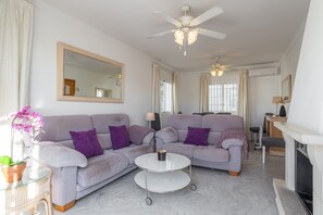 Een woonkamer met een bank, een salontafel, een plafondventilator en een open haard.