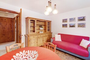 A room with a wooden cabinet, a red sofa, and a dining table with chairs.