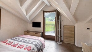 Un dormitorio con una cama, un aparador de madera, un televisor montado en la pared y un balcón con vistas al campo.