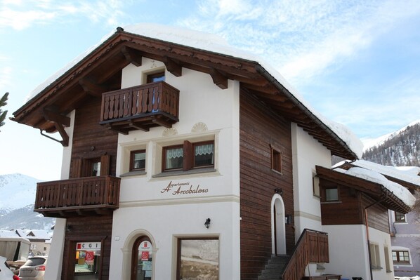 A two-story building with a wooden balcony, a sign reading 'Aquilamonti Arcabalo,' and a visible entrance.