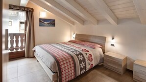 Un dormitori amb sostre inclinat, un llit amb edredó estampat, una tauleta de nit i una làmpada penjada a la paret.