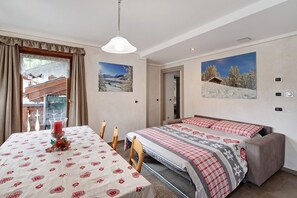 Une chambre à coucher avec un lit, une table et des chaises, une fenêtre avec des rideaux et deux tableaux accrochés au mur.