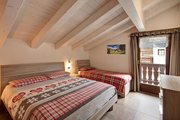 Une chambre avec un plafond en bois, deux lits avec une literie rouge et blanche, une table de chevet et une fenêtre avec des rideaux.
