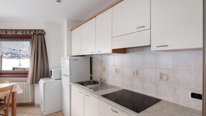 Una cocina con armarios blancos, encimera negra, un lavamanos y una ventana con cortinas.