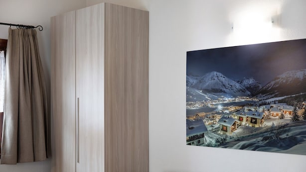 Une pièce avec une grande armoire, un tableau encadré représentant une ville de montagne enneigée et un canapé.