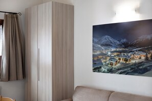 Ein Zimmer mit einem großen Kleiderschrank, einem gerahmten Bild einer verschneiten Bergstadt und einem Sofa.
