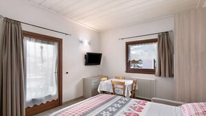 Une chambre à coucher comprenant un lit, un bureau, une chaise, un téléviseur et une fenêtre avec des rideaux.
