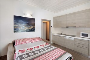 Une chambre à coucher avec un lit, un tableau, une cuisine équipée d’armoires et un four à micro-ondes.