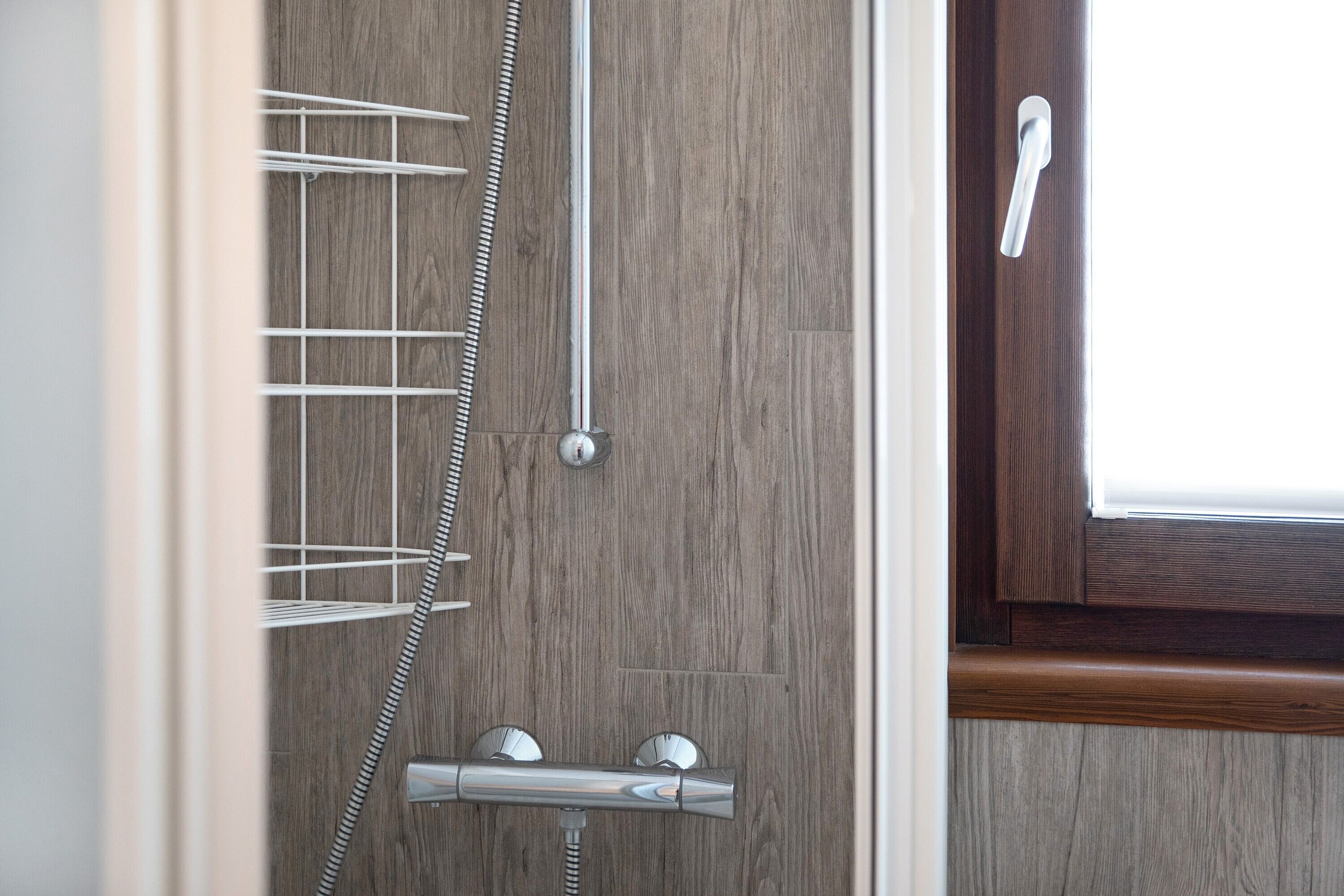 Una doccia con un tubo flessibile cromato e manopole di controllo, una parete in legno e una porta con maniglia.