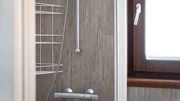 Una doccia con un tubo flessibile cromato e manopole di controllo, una parete in legno e una porta con maniglia.