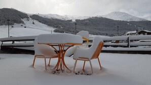 Un espace extérieur aménagé avec des tables et des chaises, recouvert de neige, et offrant une vue sur un paysage montagneux enneigé.