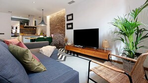Una sala de estar moderna con un sofá, un televisor, una zona de comedor y una cocina al fondo.