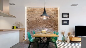Un comedor con pared de ladrillo, lámpara colgante, mesa de madera con sillas verdes y un moderno mueble para televisor.