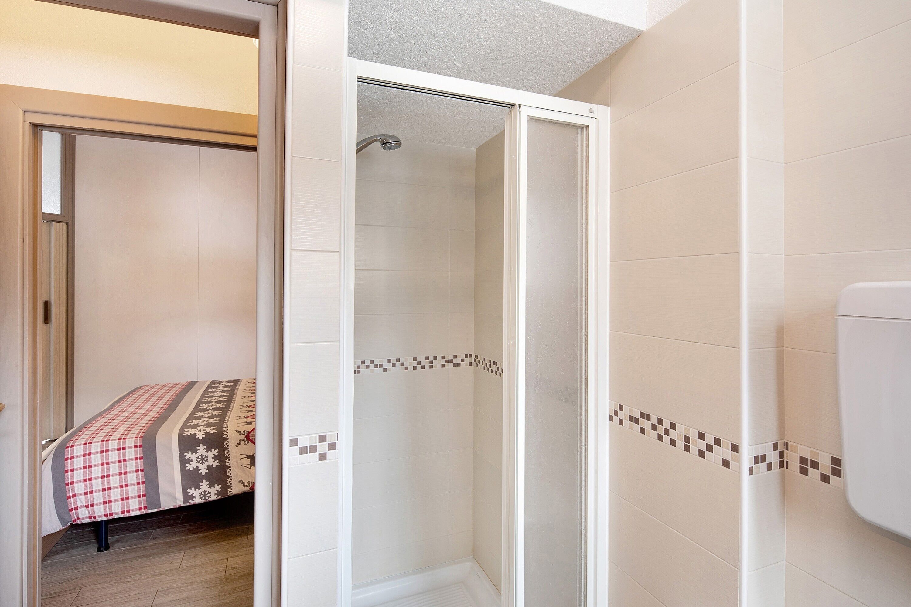 Un bagno con doccia, wc e un letto con copripiumino a quadretti.