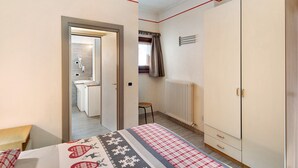Een slaapkamer met een bed, een kledingkast, een radiator en een badkamer zichtbaar door een geopende deur.