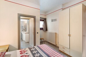 A bedroom with a bed, a wardrobe, a radiator, and a bathroom visible through an open door.
