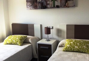 Habitación de hotel con dos camas, cada una con un cojín estampado, una mesita de noche con lámpara y un adorno en la pared.
