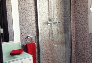 Un baño con cabina de ducha de vidrio, una toalla roja y un lavabo de vidrio con una tela roja.