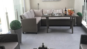 Et moderne udendørs opholdsområde med sofa, spisebord og stole, der byder på udsigt over byen.
