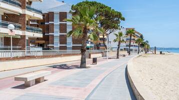 Un paseo marítimo costero con playa, palmeras y una hilera de edificios de varios pisos con balcones.