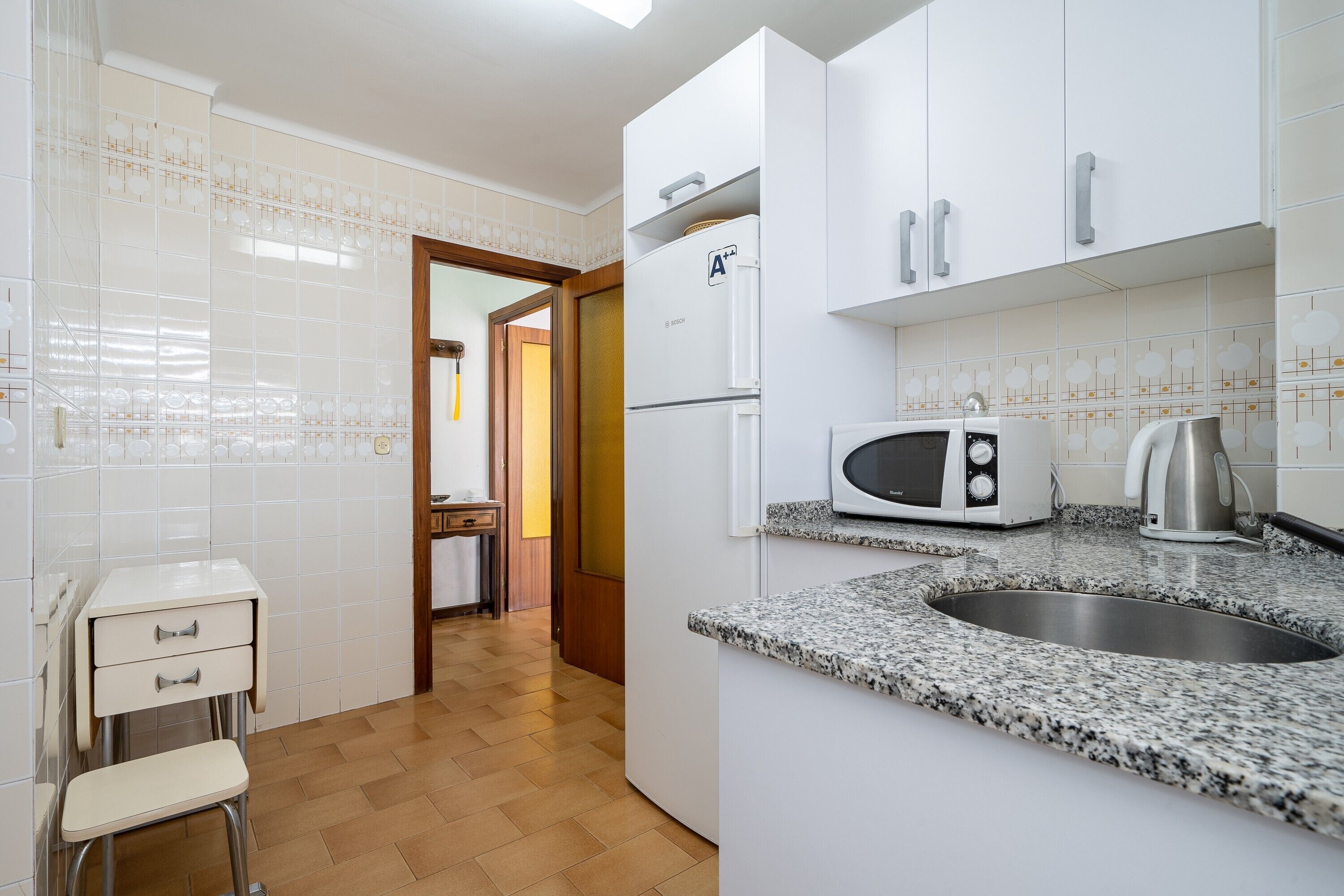 A kitchen with white cabinets, a microwave, a kettle, and a sink.