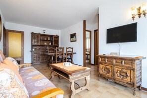 Ein Wohnzimmer mit einer Couch, einem Holzkabinett, einem Fernseher und einem Essbereich mit Stühlen und einem Tisch.